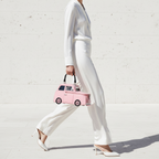 Woman in a white outfit holding a pink handbag against a white background