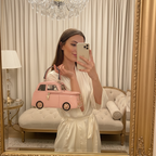 Woman taking a mirror selfie in a luxurious room with a chandelier and pink car-shaped bag.